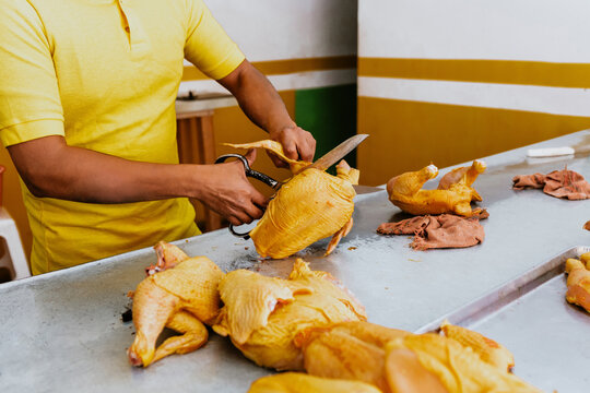 hispanic Male hands of Poultry vendor with raw chickens being sliced by the Pollero at Chicken shop or Polleria in Mexican market in Mexico Latin America