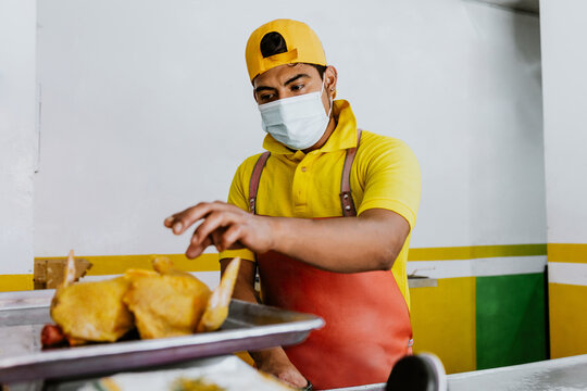 hispanic Male Poultry vendor wearing facemask with raw chickens being sliced by the Pollero at Chicken shop or Polleria in Mexican market in Mexico Latin America