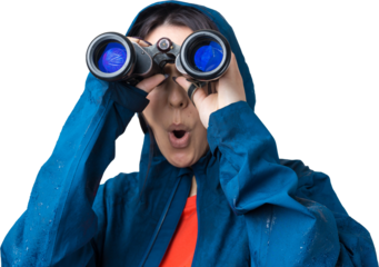 A tourist girl in a blue raincoat holds binoculars in her hands and looks into the distance, spies.