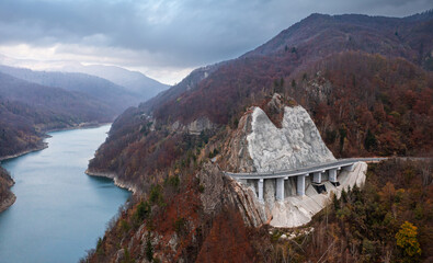 Amazing aerial view of a cliff coast road through mountains and autumn forests next to a lake Siriu...