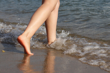 Barefoot woman running by the sand in the sea waves. Naked female legs in water, beach vacation