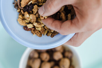 a man's hand takes one peeled piece of walnut from a blue bowl