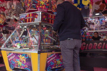 amusement park in the city, a machine for playing with coins, a man stands with his back to the camera, plays the machine, wants to win a toy, gambling
