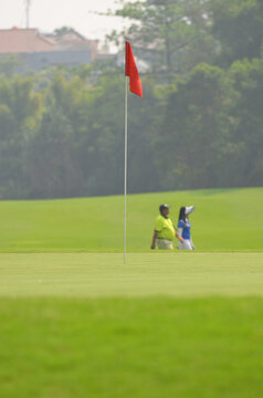 Golf flag on putting green with background blurry photo of a male golfer with a female caddy walking behind it. 