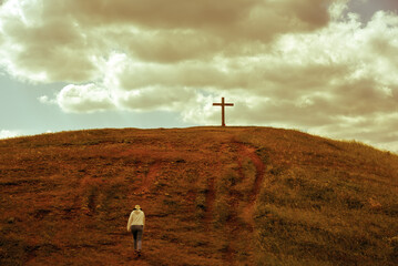 Person walking towards a cross on the hill - obrazy, fototapety, plakaty