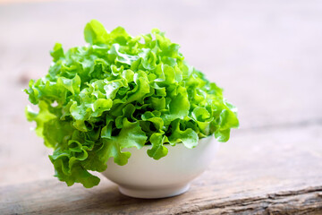 Fototapeta premium Leafy greens or lettuce in a white bowl on a wooden background is a food that adds fiber to the body. Healthy food concept.