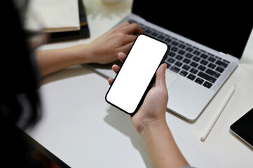 Close-up image of a female offie worker using her smartphone while using laptop at her desk