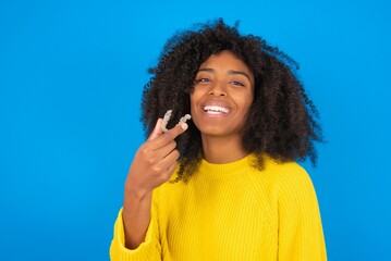 young woman with afro hairstyle wearing orange crop top over blue wall holding an invisible aligner ready to use it. Dental healthcare and confidence concept.