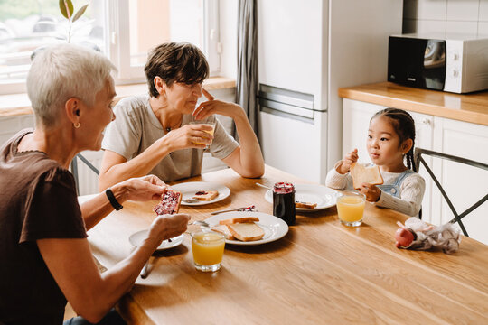 Two mature women with cute little asian girl eating toasts