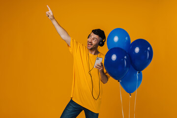 Cheery man listening music with headphones and smartphone and pointing finger at copy space while...