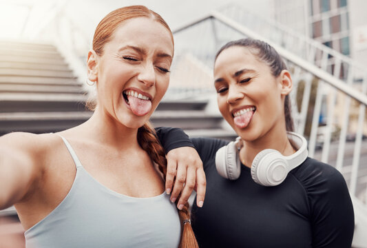 Women, friends selfie and tongue in city for training, comic time or funny face with headphones in profile picture. Woman workout group, exercise photo or social media by stairs in metro with support