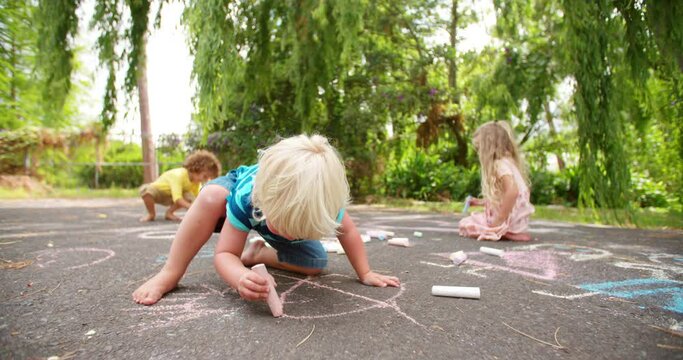 Little boy thinking about what chalk picture to draw next on a walkway in a park