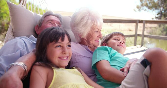 Loving grandparents spending time sitting with their grandchildren on their porch on  a summer holiday in Slow Motion