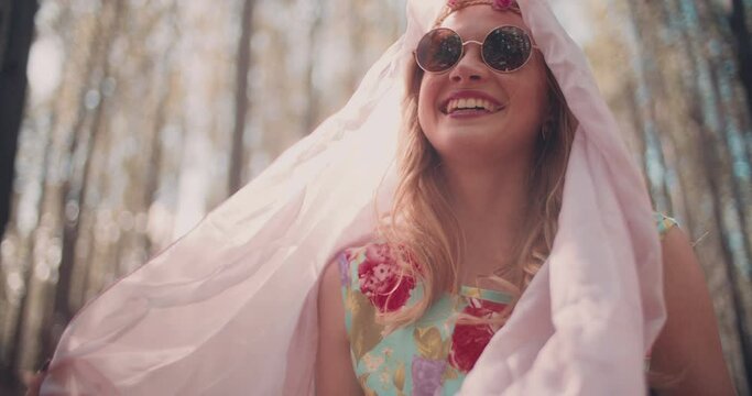 Low angle boho fashion shot of a girl in a summer forest with sun flare behind her, playing with material  in Slow Motion