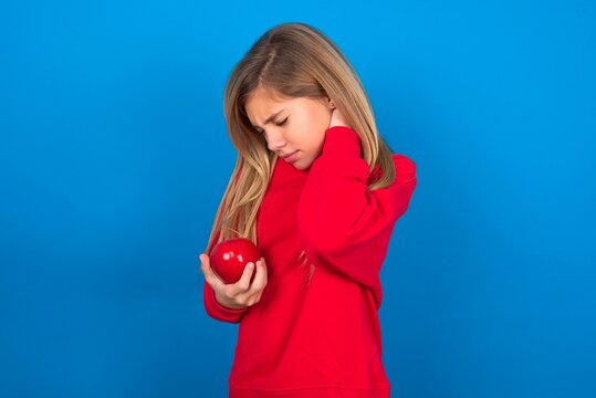 Caucasian Teen Girl Wearing Red Sweater Over Blue Studio Background Suffering From Back And Neck Ache Injury, Touching Neck With Hand, Muscular Pain.