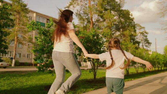 mother daughter run through park summer day. happy family. girl running with her mother on pavement of the road. fun school holidays. little child with parent on a walk outdoors. happy family concept