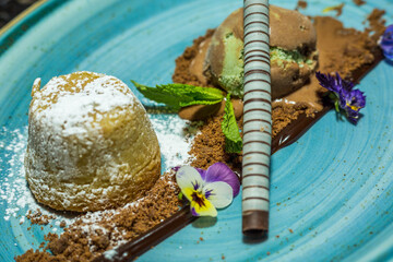 En un recipiente dos bolas de helado pistacho y chocolate acompañado con una barra de chocolate.