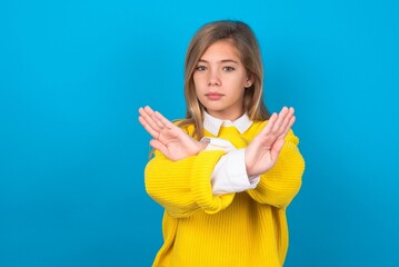 caucasian teen girl wearing yellow sweater over blue studio background has rejection expression...