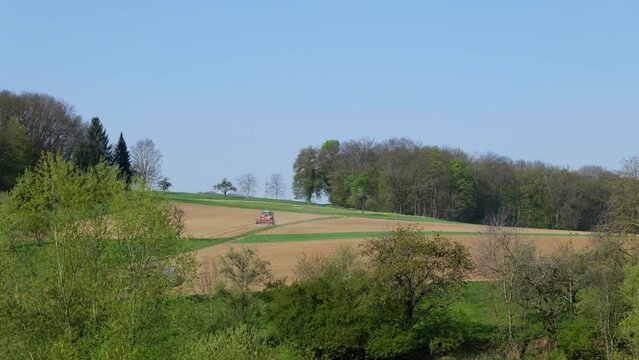 Traktor auf Feld im Fr&uuml;hling nahe Wald