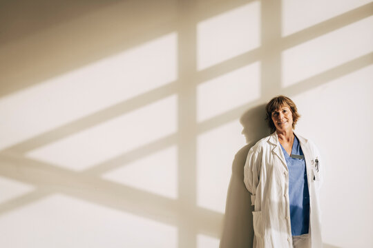 Portrait of mature female doctor standing against wall with shadow
