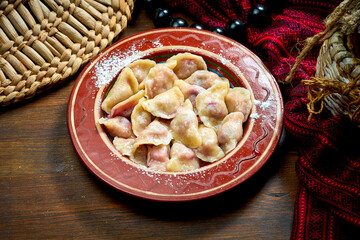 Traditional Ukrainian sweet varenyky with cherries and powdered sugar in a clay dish. Ukrainian cuisine