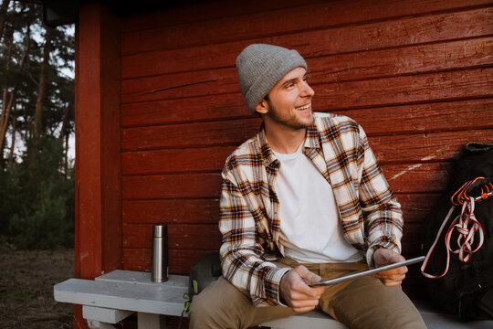 Cheerful man using tablet while sitting on bench in forest