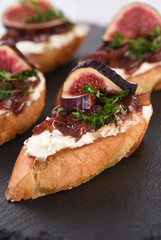 Canape or crostini with toasted baguette, cream cheese, onion jam, figs and fresh thyme on a slate board. Perfect as an aperitif for a holiday or party.