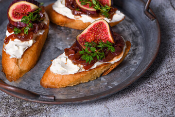 Canape or crostini with toasted baguette, cream cheese, onion jam, figs and fresh thyme on a slate board. Perfect as an aperitif for a holiday or party.