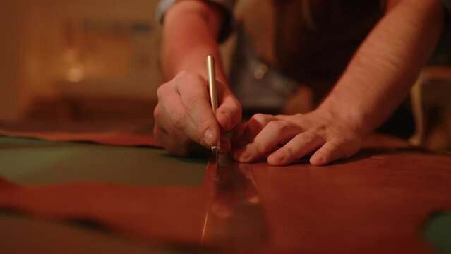 Craftsman shoemaker cutting genuine leather with knife scalpel on table. Leatherworker at work making handmade shoes.