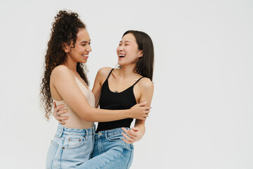 Naklejka premium Two pretty girls smiling at each other while posing isolated over white wall