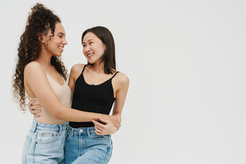 Beautiful multinational girls smiling and hugging while standing over isolated white background