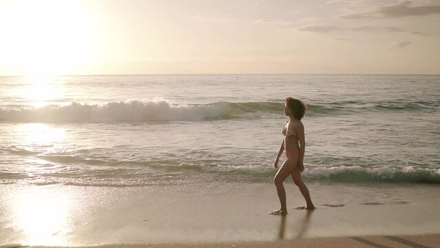 Dolly shot of woman in bikini walking on shore at beach against sky during sunset
