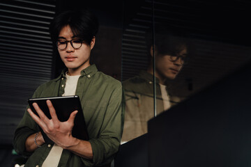 Asian business man working on tablet computer while standing in office