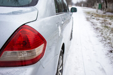 Fototapeta premium Winter road.Driving in winter.Side view of the car.Wet body.Rear headlight of the car.Snow-covered road.Outside the car.Rent a car.Driving school.Road into the distance.Winter.Red headlight.Automotive