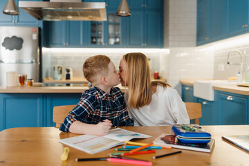 Mother kissing her son while sitting at table together in kitchen