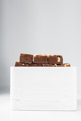 Pieces of chocolate fudge in a white metal tin, homemade chocolate peanut fudge stacked in a metal tin