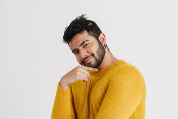 Pensive indian guy touching his chin and looking at camera while standing isolated