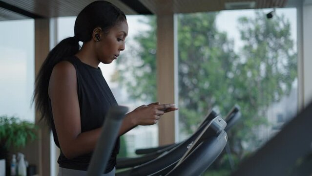 Young woman using her phone in a treadmill in slow motion with ear phones