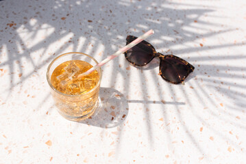 Iced drink with paper straw and sunglasses under a palm tree