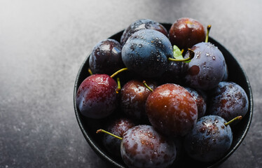 Close up of bowl of fresh picked plums on black background.