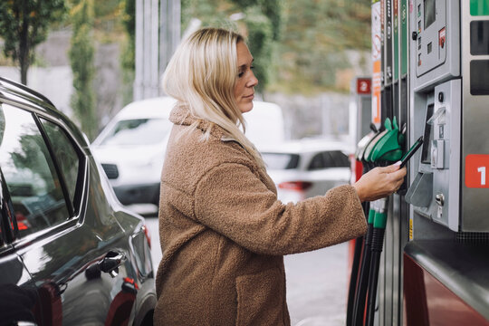 Side view of blond woman doing payment via smart phone while standing at fuel station