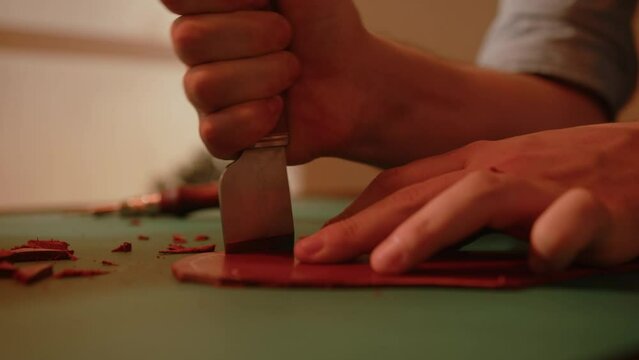 Artisan shoemaker processes piece of leather with saddlery knife. Craftsman making handmade shoes.
