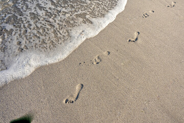 Bare footprints on a sandy shore about to be washed away by a wave. Hermanus, Whale Coast, Overberg, Western Cape, South Africa.