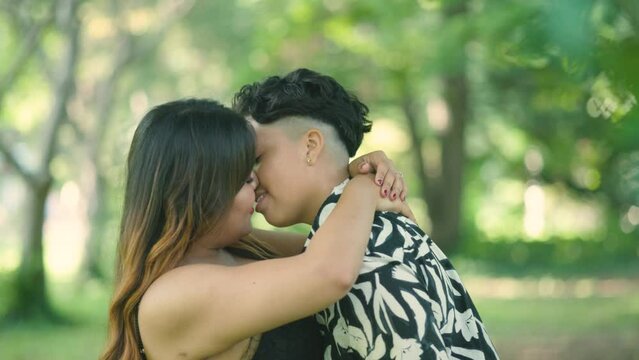 Two Latin lesbian women kiss in park, showcasing love and diversity. Ideal for LGBTQ+ advocacy projects. Slow-motion captures unity, inclusiveness, and diversity in a symbol of love and acceptance.