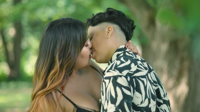 Two Latin lesbian women share a romantic kiss in park,. Love and diversity. Ideal for LGBTQ+ advocacy projects. Slow-motion shots depict unity, and  inclusiveness in a symbol of love and acceptance.