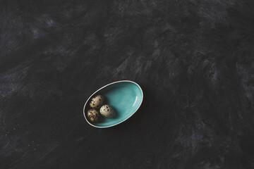 Quail eggs in blue ceramic plate on rustic black background