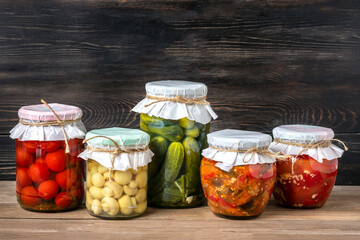 Fototapeta na wymiar Homemade pickled cherry tomatoes, cucumbers, champignons, garlic, eggplant, red peppers in jars on wooden shelf Homemade canned and fermented foods concept Seasonal product