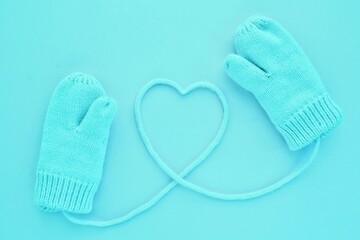 Close-up blue mittens and heart symbol shaped of string on blue background. Lifestyle and warm feelings concept. Valentine day. Monocolor romantic pattern. Winter theme. Flat lay composition. Top view