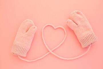Close-up pink mittens and a heart symbol shaped of string on pink background. Lifestyle and warm feelings concept. Valentine day. Monocolor romantic pattern. Flat lay composition. Top view