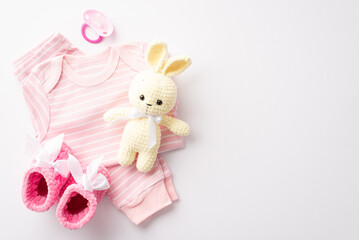 Baby shower concept. Top view photo of infant clothes pink shirt pants tiny booties pacifier and knitted rabbit toy on isolated white background with empty space